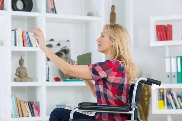 Mulher com deficiência atingindo livro de prateleira — Fotografia de Stock
