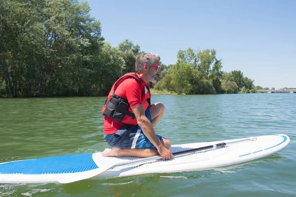 Maduro atraente cavaleiro contemplando natureza sentado no paddle board — Fotografia de Stock