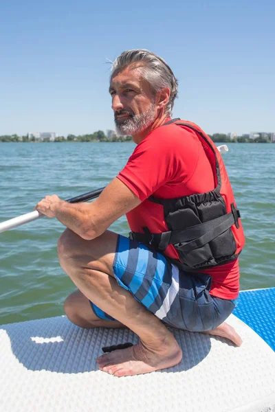 Maduro atraente cavaleiro contemplando natureza sentado no paddle board — Fotografia de Stock