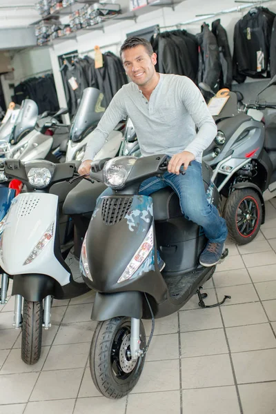 Uomo seduto su scooter moderno in negozio — Foto Stock