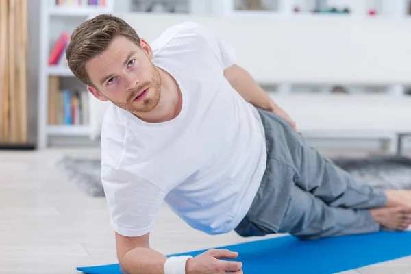 Adulto joven haciendo ejercicio sobre una esterilla en su apartamento —  Fotos de Stock