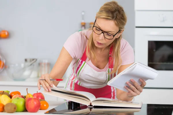 Reife Frau liest Kochbuch in der Küche auf der Suche nach Rezept — Stockfoto