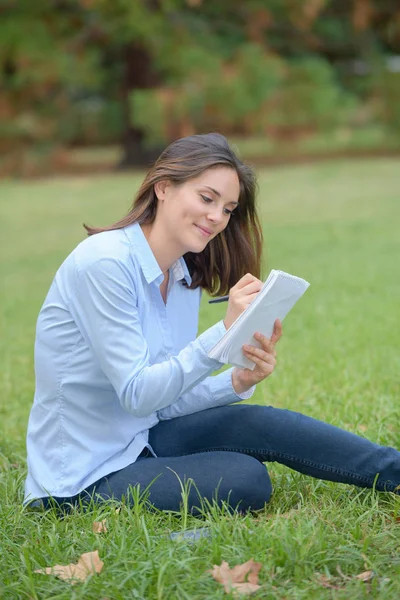 Mujer sentada en el parque escribiendo en bloc de notas —  Fotos de Stock