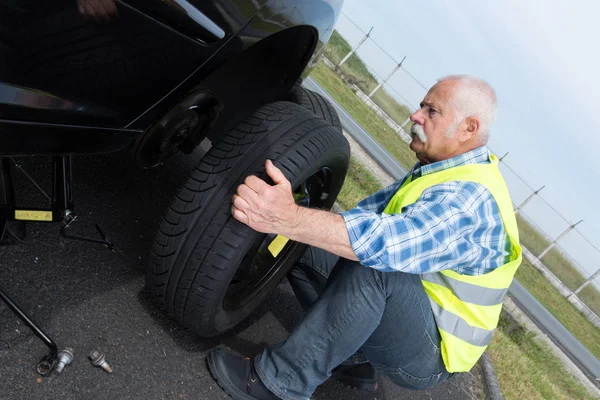 Homem idoso mudando pneu vazando na beira — Fotografia de Stock