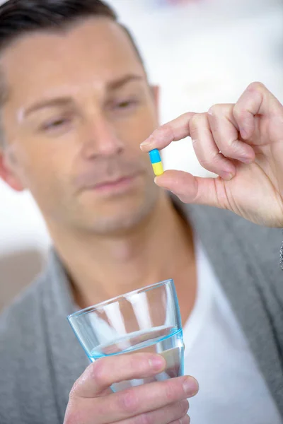 Человек держит капсулу таблетки и стакан воды — стоковое фото