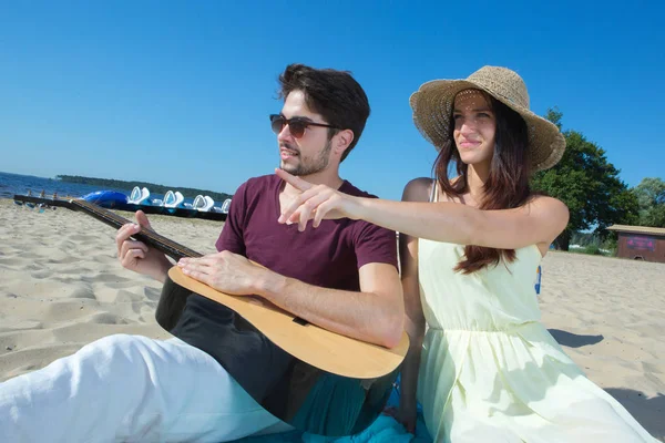 Gitarı ve kız arkadaşı sahilde olan genç bir adam. — Stok fotoğraf