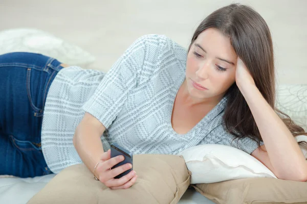 Lady liggande på soffan tittar på mobiltelefon, sorgligt uttryck — Stockfoto