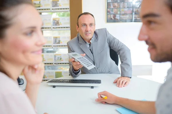 Fastighetsmäklare anläggning kalkylator mot unga par — Stockfoto