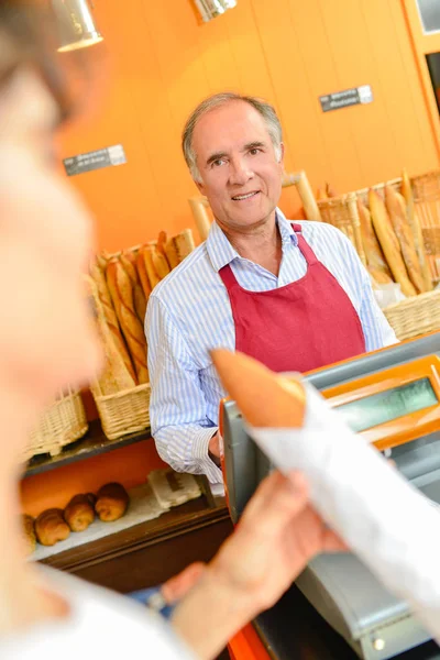 Baker porci bageta k zákazníkovi — Stock fotografie