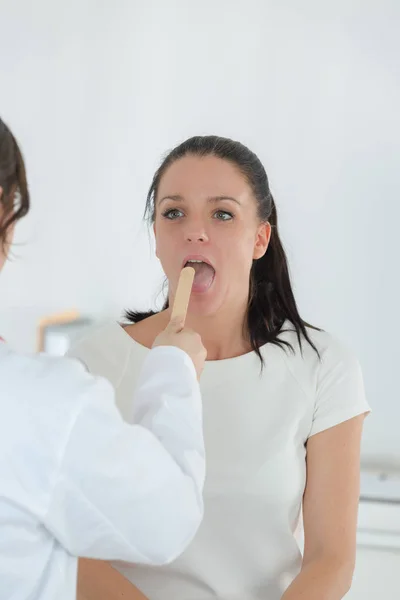 Doctor examining tongue and throat of female patient — Stock Photo, Image