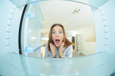 Woman with shocked expression looking inside empty fridge clipart