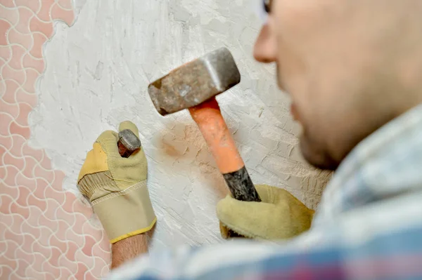 Человек снимает плитку со стены молотком и долотом — стоковое фото