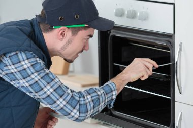 young repairman in overall installing brand new oven in kitchen clipart