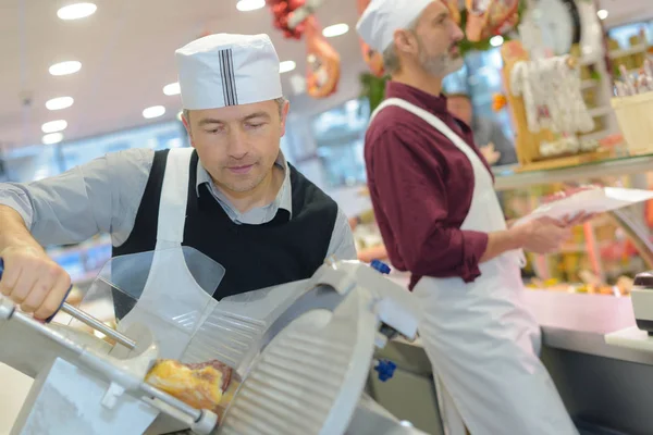 Homme tranchant de la viande au comptoir de charcuterie — Photo