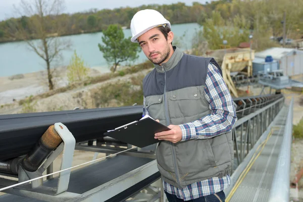 Man håller Urklipp bredvid utomhus transportband — Stockfoto