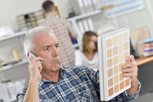 Mannen på telefon med skeptiska uttryck, hålla färgkartor — Stockfoto