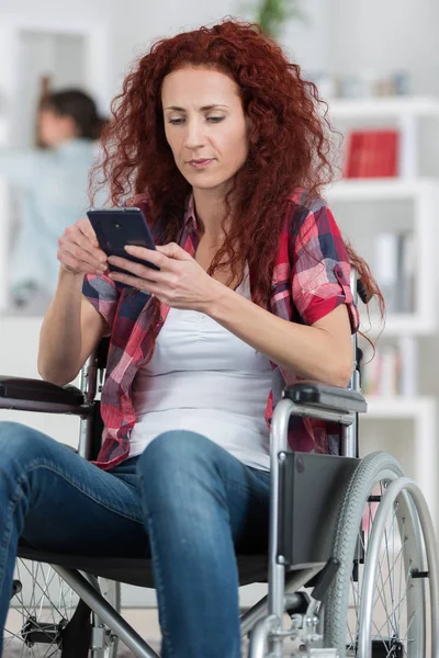 Handicapped redhead woman texting and surfing on her smartphone — Stock Photo, Image