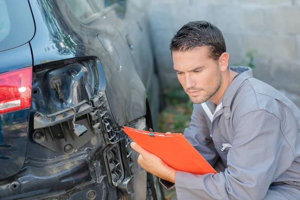 Joven mecánico inspeccionando un coche dañado — Foto de Stock
