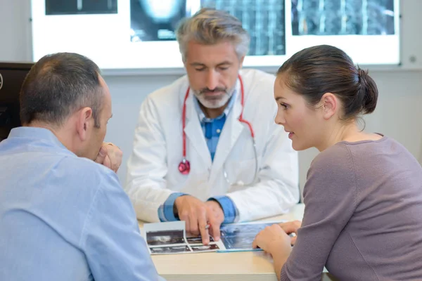 Arzt schaut sich mit Paar Röntgenbilder an — Stockfoto