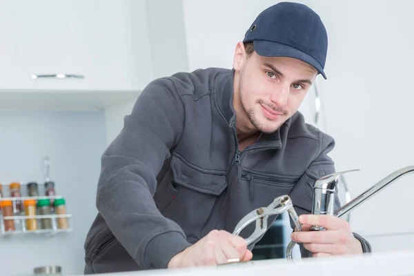 Handsome young plumber fixing tap at cleints home — Stock Photo, Image