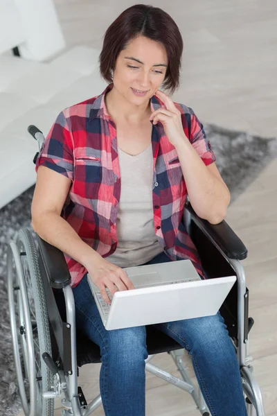 Gehandicapte vrouw in rolstoel met laptop thuis — Stockfoto