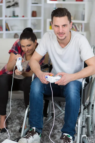 Νεαρό ζευγάρι παίζει βίντεο παιχνίδια στο σπίτι ο φίλος σε αναπηρικό καρότσι — Φωτογραφία Αρχείου