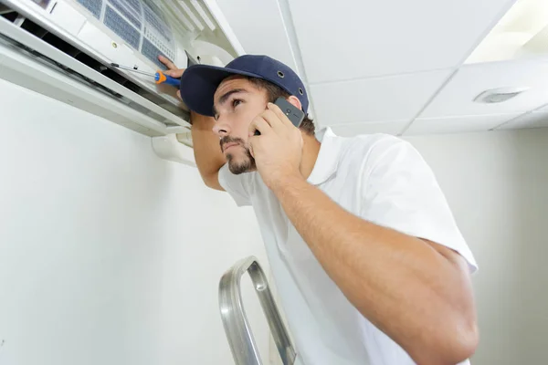 Jovem faz-tudo reparar o sistema de ar condicionado pedindo ajuda — Fotografia de Stock