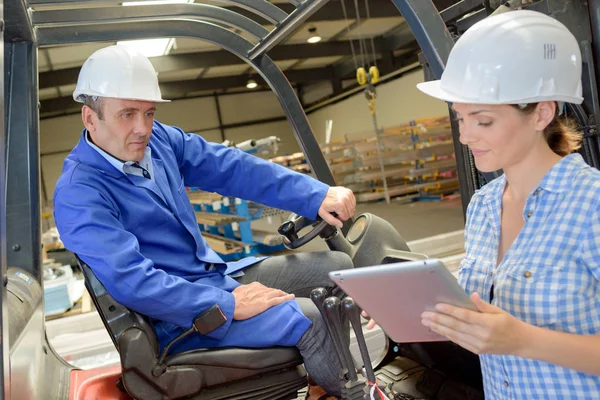 Vrouw met behulp van Tablet PC naast man op heftruck — Stockfoto