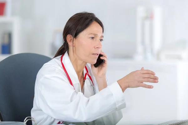 Dentiste féminine grave regardant le rapport tout en utilisant un téléphone portable — Photo