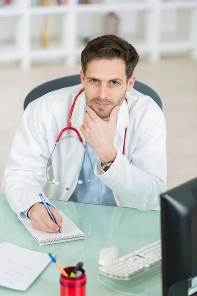 Atractivo joven médico escribir prescripción sentado en el escritorio — Foto de Stock