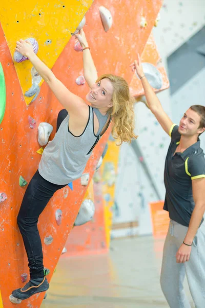 Instruktör vägledande kvinna på rock klättervägg på gymmet — Stockfoto