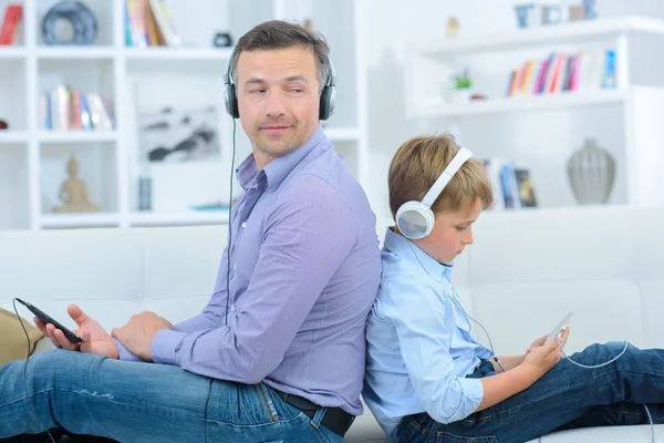 Vader en zoon koptelefoon, rug aan rug dragen — Stockfoto