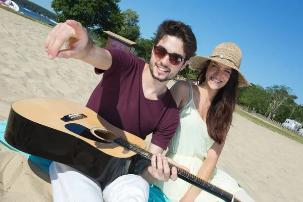 Młody człowiek ze swoją gitarą i dziewczyną na plaży — Zdjęcie stockowe