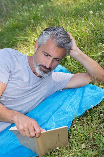 Man lyingsitting in the grass reading a book — Stock Photo, Image