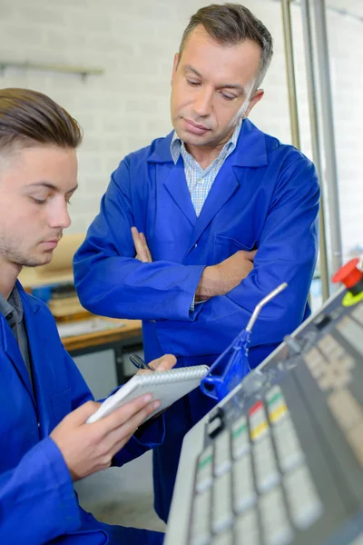 Supervisor watching younger worker writing notes — Stock Photo, Image