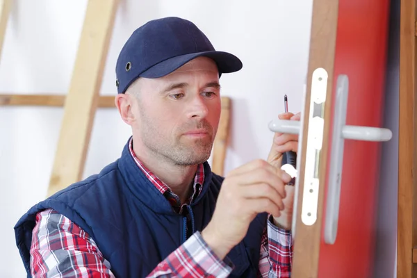 Carpintero con cerradura durante la instalación del proceso de bloqueo en la puerta de madera — Foto de Stock
