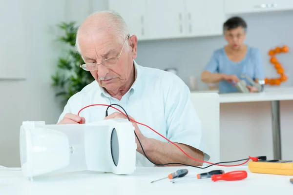 Senior male using multimeter, wife looking on — Stock Photo, Image