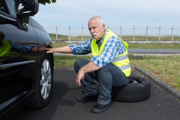 Discouraged senior man attempting to change a tyre — Stock Photo, Image