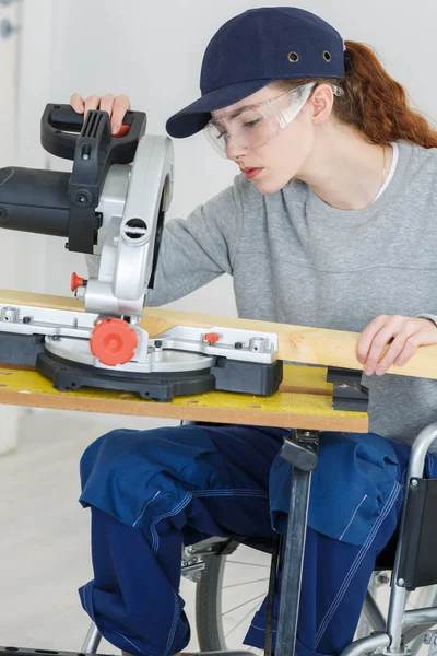 Mujer joven en silla de ruedas usando sierra circular — Foto de Stock