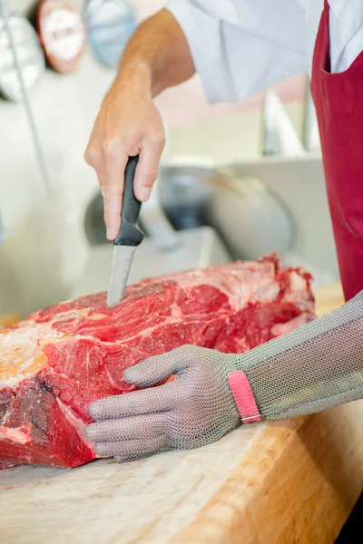 Homem cortando grande pedaço de carne, vestindo luva protetora — Fotografia de Stock