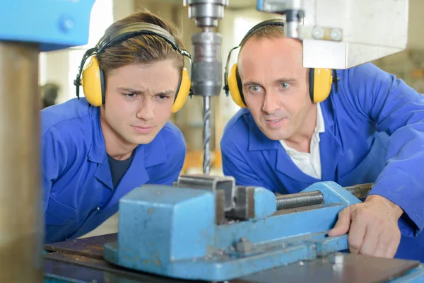 Joven hombre viendo ingeniero uso banco taladro — Foto de Stock