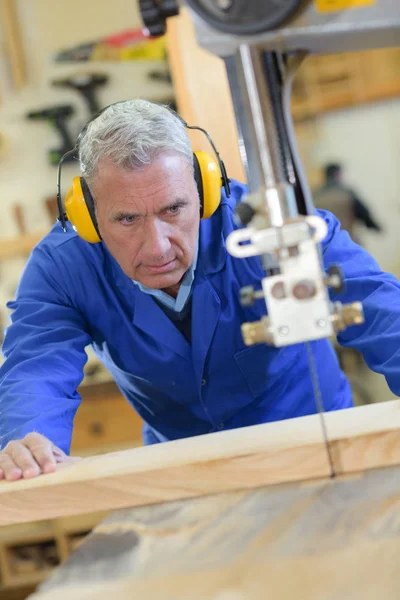 Hombre mayor que usa protectores de oídos mientras usa sierra de mesa — Foto de Stock