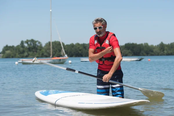 Man naast een stand-up paddle board op het meer — Stockfoto