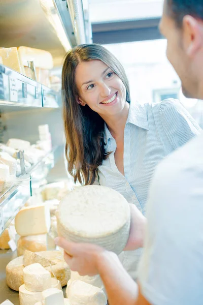 Mužské shop pracovník ukazující celý sýr k zákazníkovi — Stock fotografie
