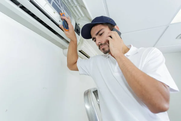 Jonge klusjesman herstellen airconditioningsysteem bellen voor hulp — Stockfoto