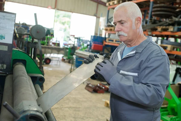 Homem sênior alimentando metal na máquina — Fotografia de Stock