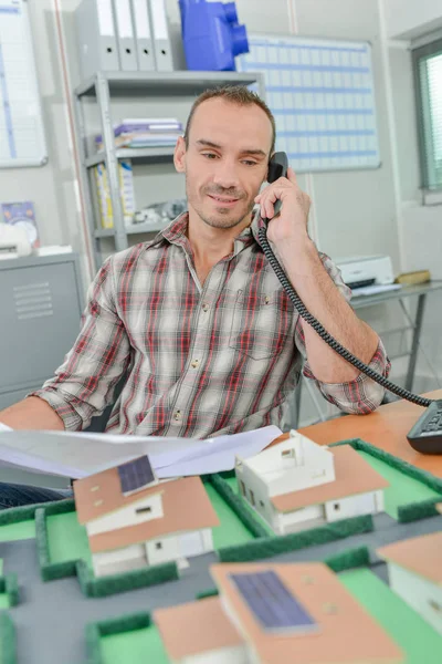 Homem ao telefone, casas modelo à sua frente — Fotografia de Stock