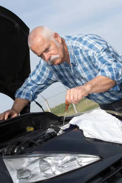 Older man checking levels and servicing his car — Stock Photo, Image