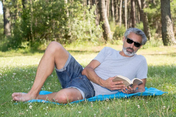 Adam lyingsitting bir kitap okuma çim — Stok fotoğraf