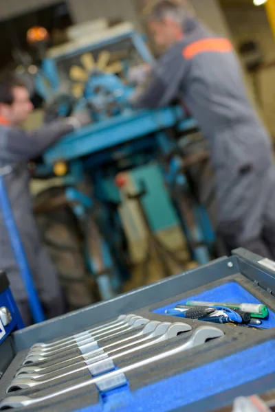 Set of spanners in foreground, mechanics at work behind — Stock Photo, Image
